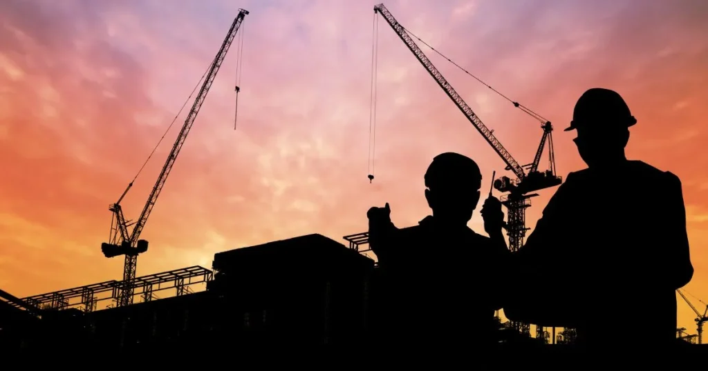 Silhouette of construction workers and cranes at sunset symbolizing industry growth and innovation.