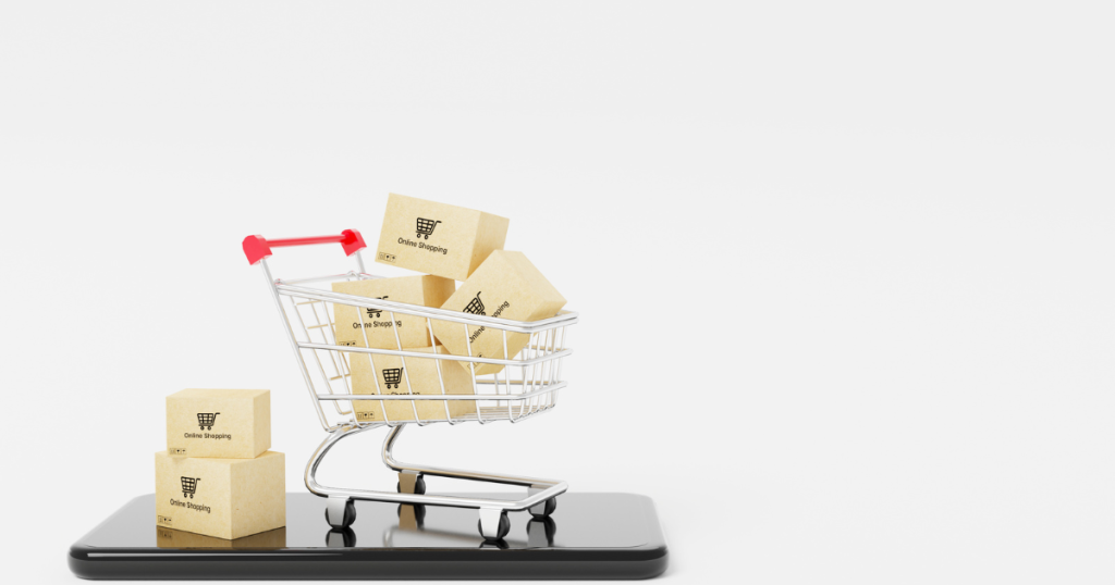 A miniature shopping cart filled with boxes labeled 'Online Shopping' placed on a smartphone, representing digital B2B eCommerce website development.